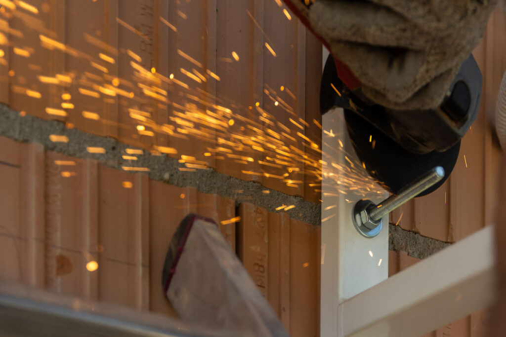 Cięcie śruby szlifierką kątową z iskrzeniem na tle muru – fotografia przemysłowa Wrocław