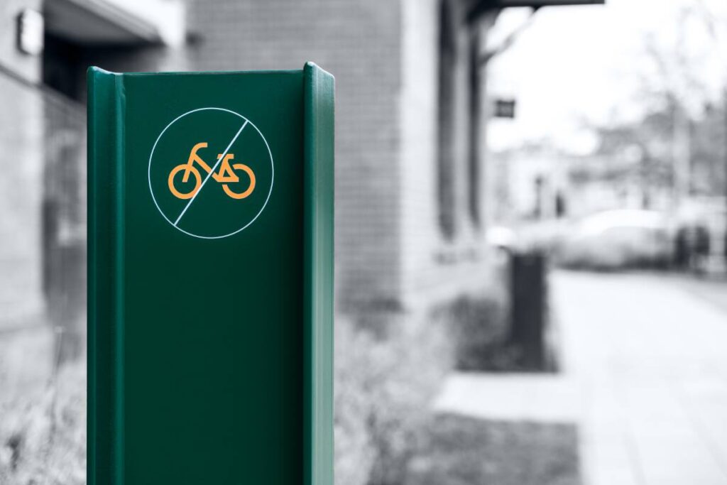 Zielony słupek z oznaczeniem zakazu jazdy rowerem na tle miejskiej zabudowy - Fotografia Inwestycji i Architektury Wrocław