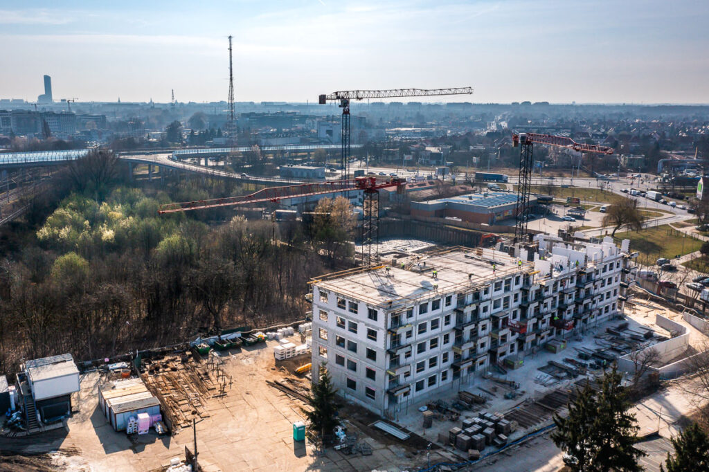 Budowa wielopiętrowego budynku mieszkalnego z widocznymi dźwigami i robotnikami – Fotografia Inwestycji Wrocław
