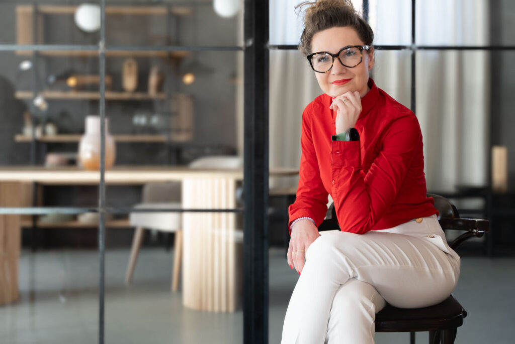 Portret kobiety w czerwonej koszuli i białych spodniach siedzącej w loftowym wnętrzu - Fotografia Biznesowa Wrocław