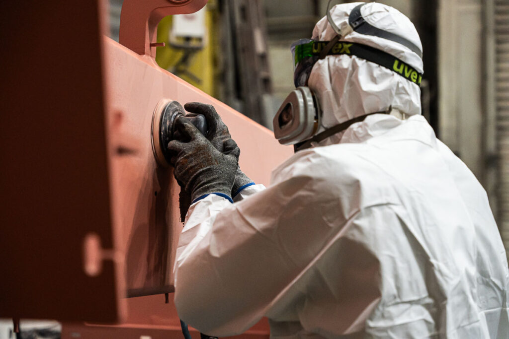 pracownik w kombinezonie ochronnym szlifujący element stalowej konstrukcji — fotografia przemysłowa Wrocław