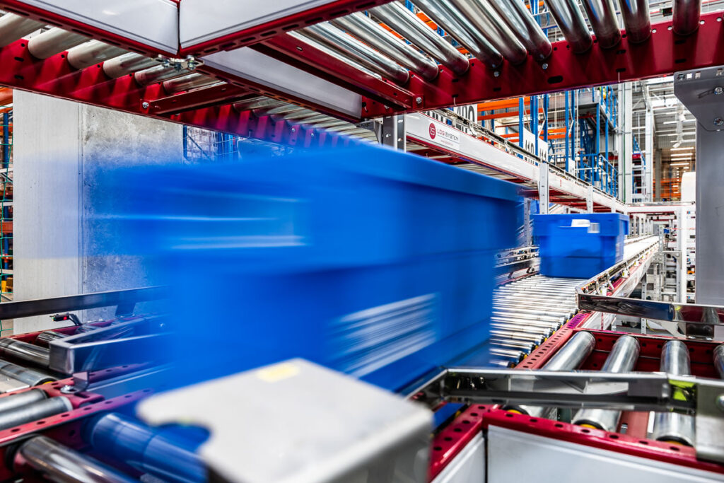 Niebieskie pojemniki w ruchu na automatycznym przenośniku rolkowym w centrum logistycznym – fotografia przemysłowa Wrocław