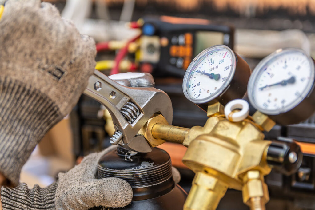 Pracownik dokręcający śrubę przy zaworze butli z manometrami – fotografia przemysłowa Wrocław
