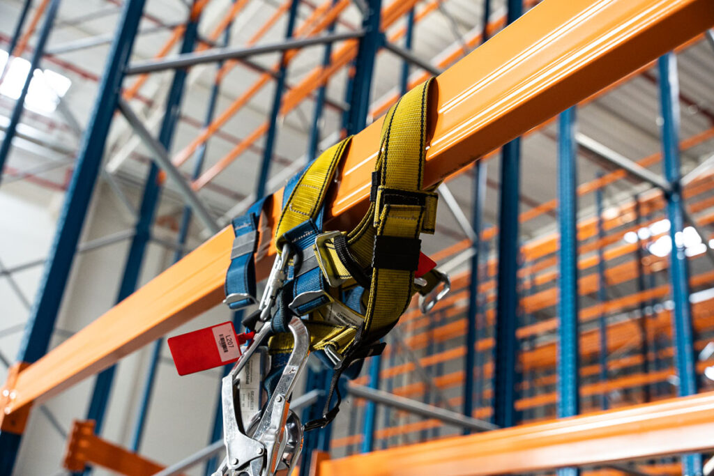 Uprząż BHP zawieszona na konstrukcji regału podczas montażu w magazynie – fotografia przemysłowa Wrocław